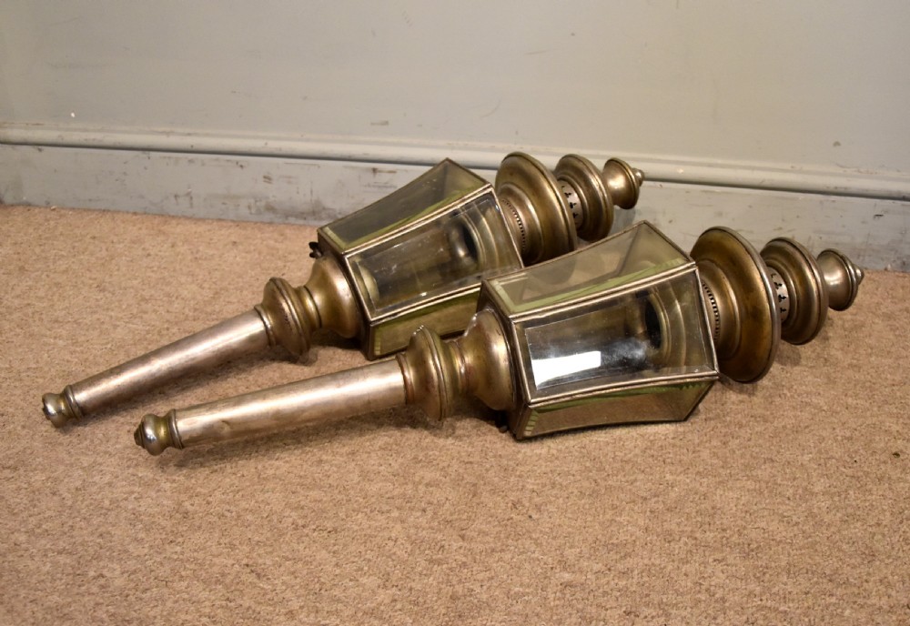 A pair of late nineteenth-century metal coaching lamps featuring glass panes, tiered upper vents, and long cylindrical mounting stems.