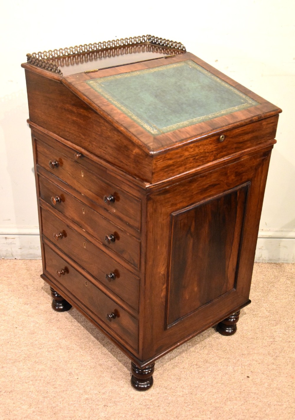 A Regency rosewood Davenport desk featuring a slanted green leather writing slope, a brass gallery rail, and four side drawers with turned wooden knobs.