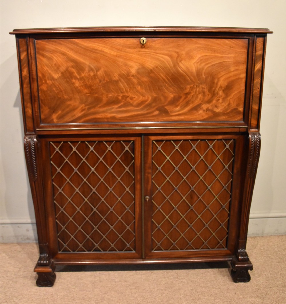 A Regency flame mahogany secretaire cabinet featuring a drop-front writing compartment above two doors with brass trellis grilles and carved pilasters.
