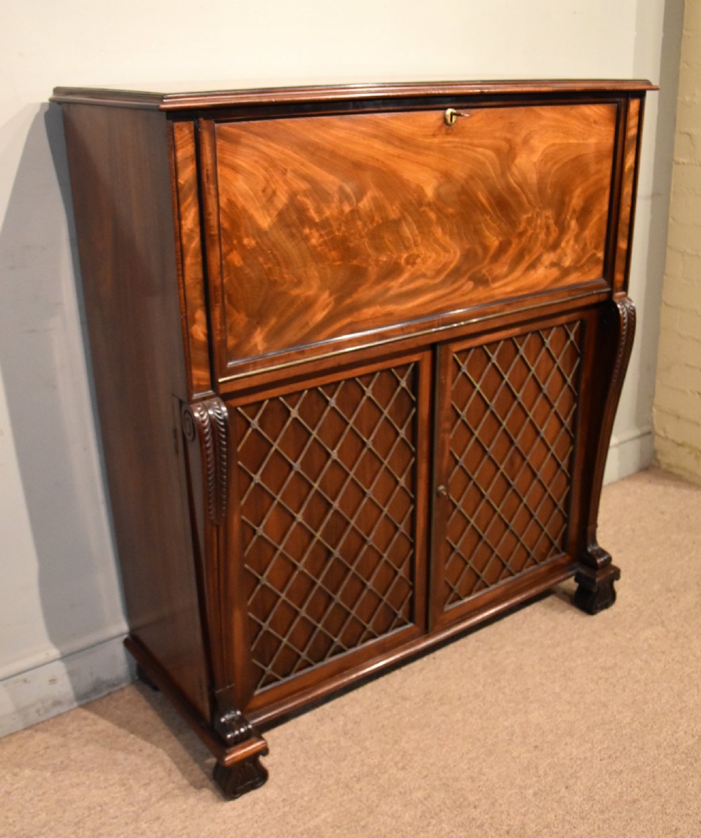 A Regency flame mahogany secretaire cabinet featuring a drop-front writing compartment above two doors with brass trellis grilles and carved pilasters. View II