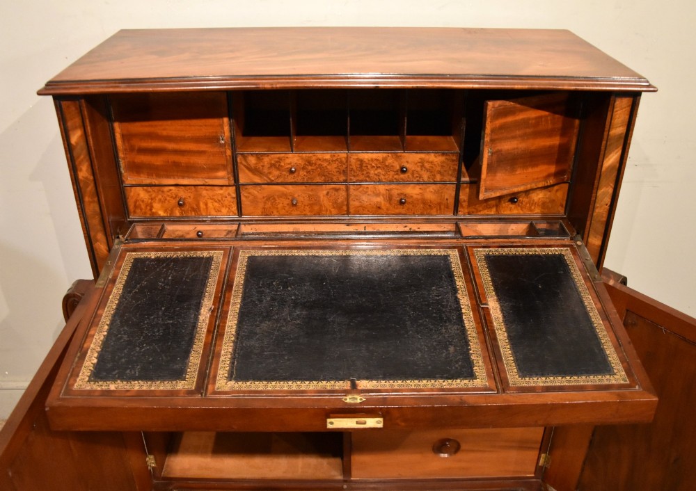 A Regency flame mahogany secretaire cabinet featuring a drop-front writing compartment above two doors with brass trellis grilles and carved pilasters. View IV