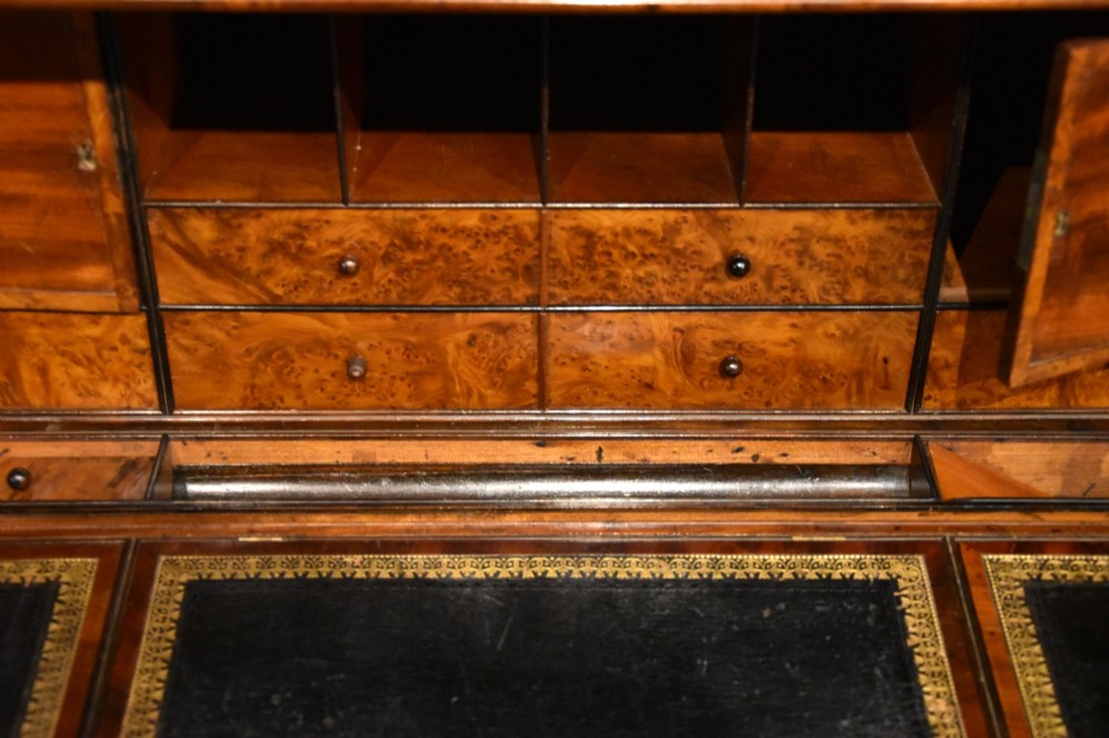 A Regency flame mahogany secretaire cabinet featuring a drop-front writing compartment above two doors with brass trellis grilles and carved pilasters. View V