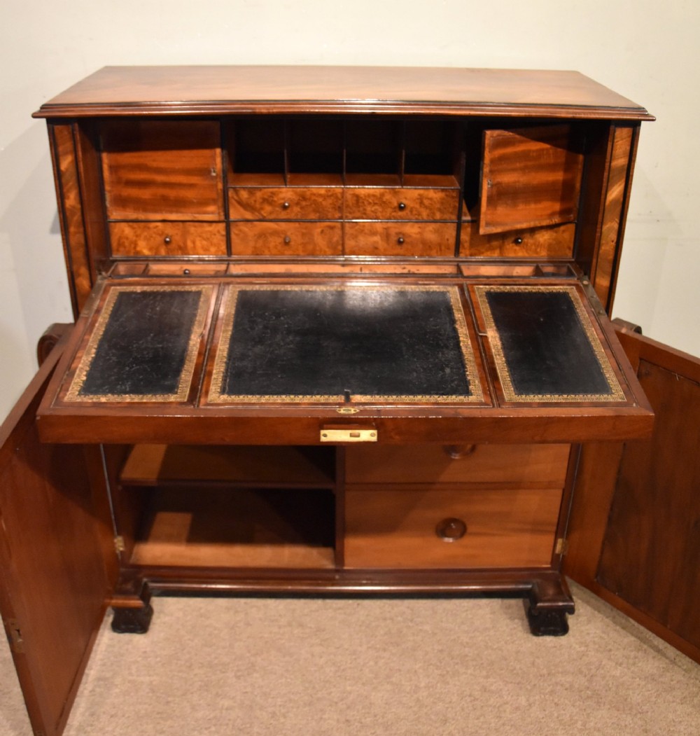A Regency flame mahogany secretaire cabinet featuring a drop-front writing compartment above two doors with brass trellis grilles and carved pilasters. View VI