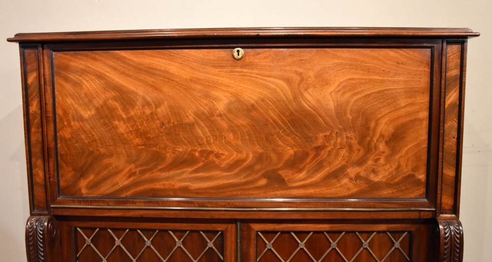 A Regency flame mahogany secretaire cabinet featuring a drop-front writing compartment above two doors with brass trellis grilles and carved pilasters. View VIII