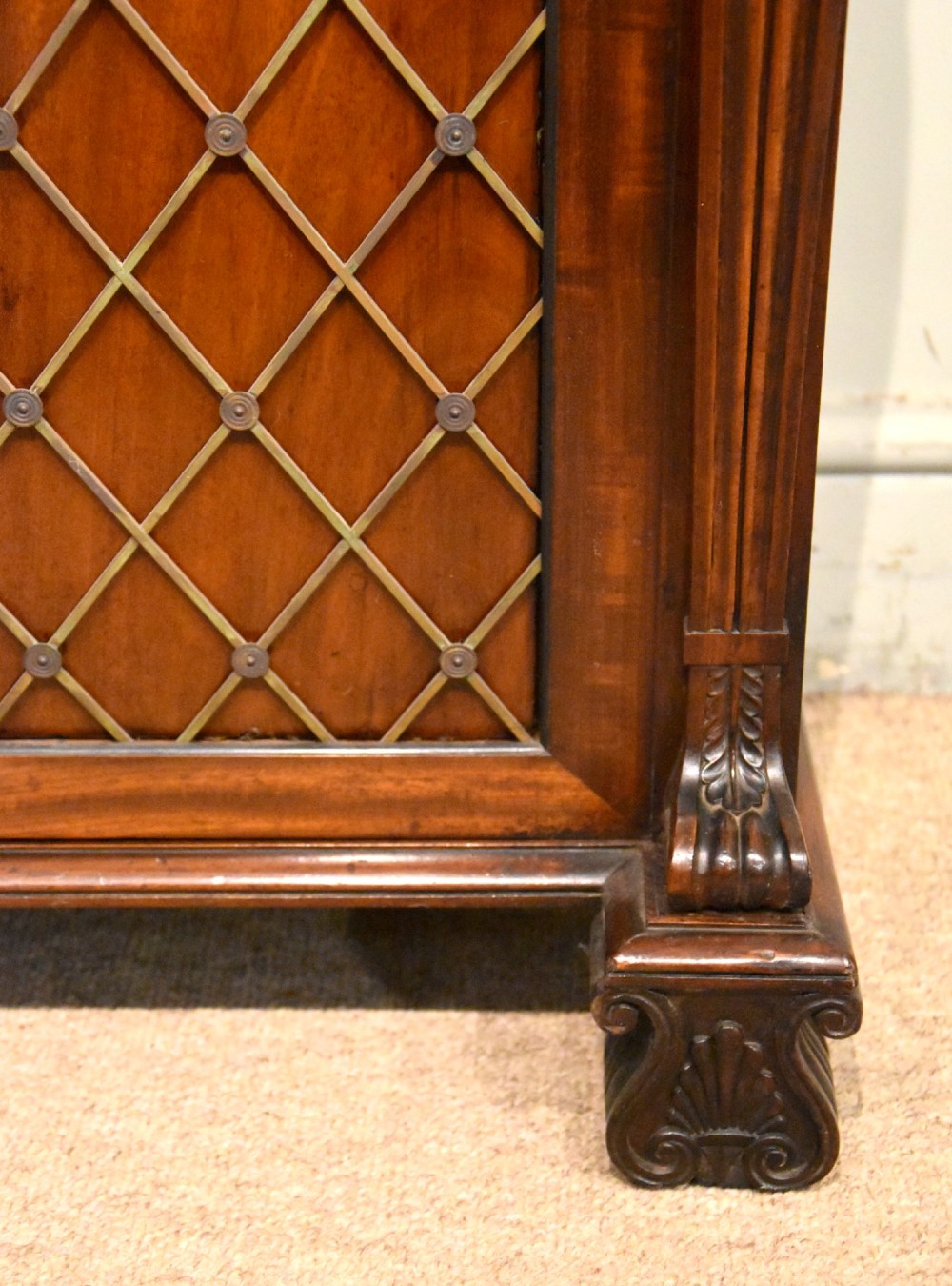 A Regency flame mahogany secretaire cabinet featuring a drop-front writing compartment above two doors with brass trellis grilles and carved pilasters. View IX