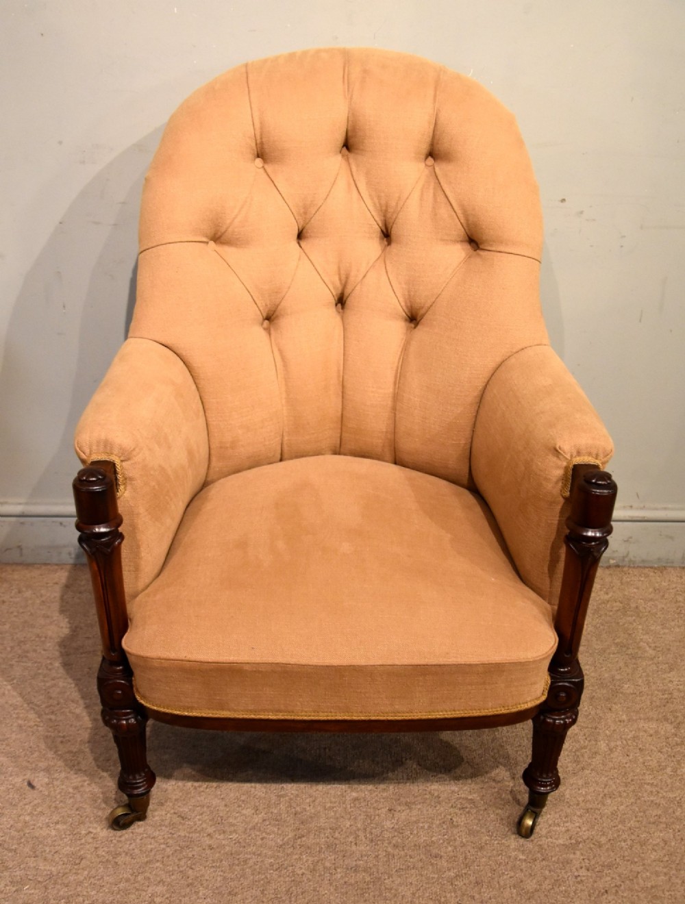 A Regency button-backed armchair upholstered in beige fabric with carved mahogany front legs on brass castors.