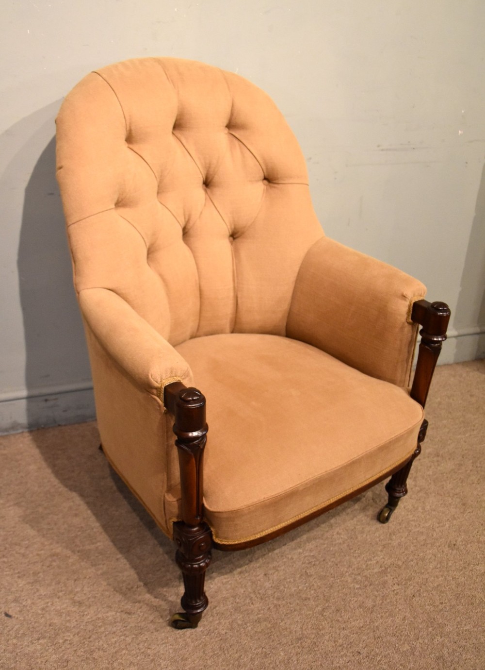 A Regency button-backed armchair upholstered in beige fabric with carved mahogany front legs on brass castors. View II