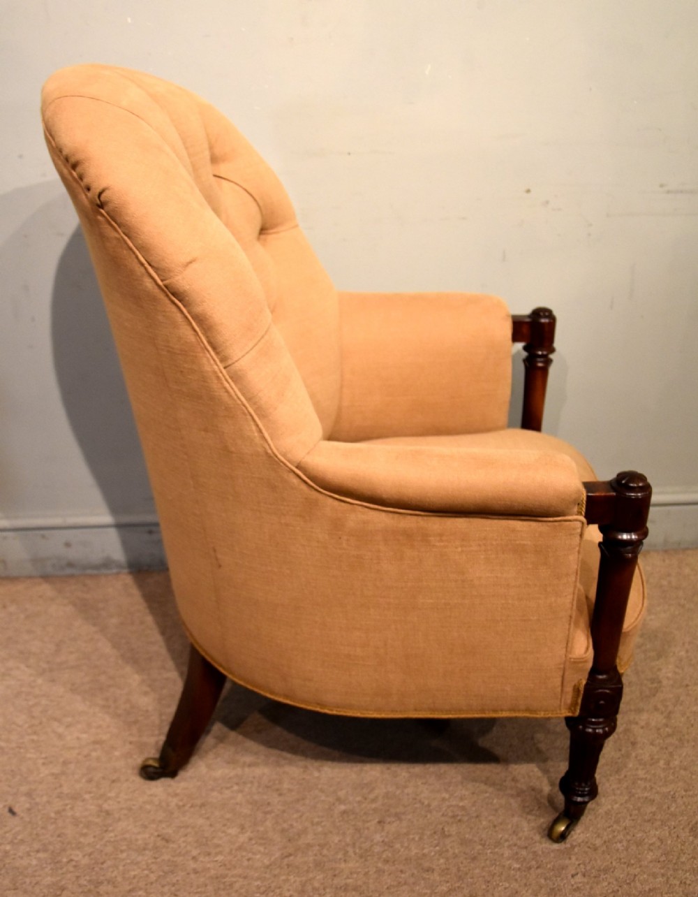 A Regency button-backed armchair upholstered in beige fabric with carved mahogany front legs on brass castors. View V