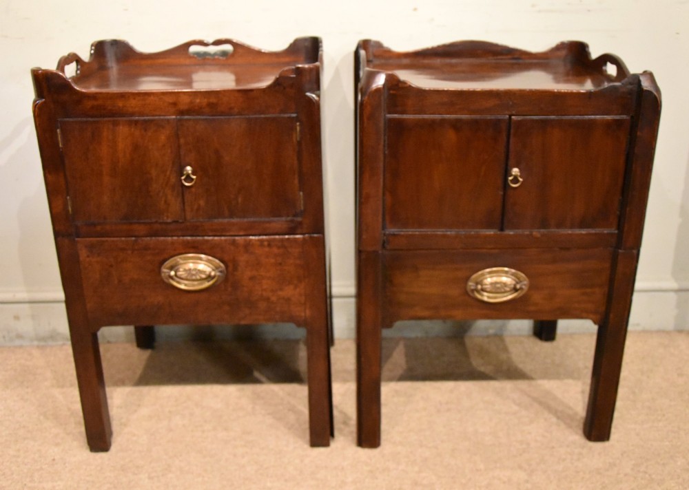 A matched pair of dark mahogany Georgian bedside cabinets, each featuring a shaped gallery top with cutout handles, a two-door cabinet, and a single lower drawer with a brass handle. View II
