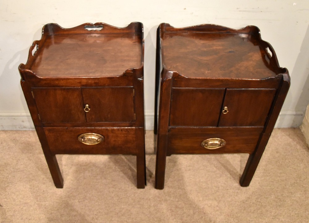 A matched pair of dark mahogany Georgian bedside cabinets, each featuring a shaped gallery top with cutout handles, a two-door cabinet, and a single lower drawer with a brass handle. View III
