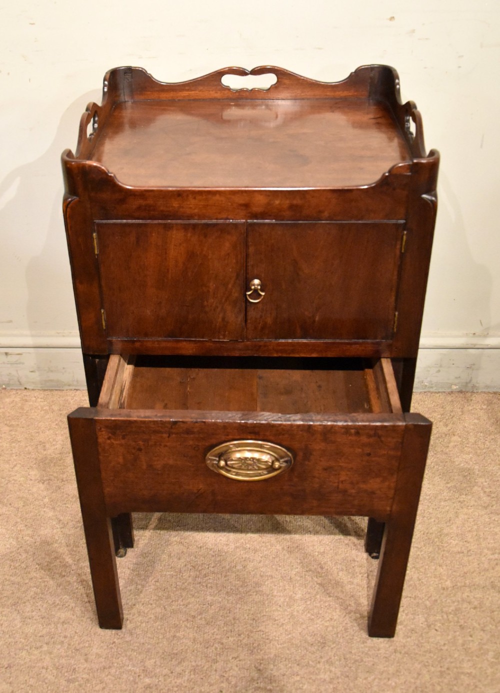 A matched pair of dark mahogany Georgian bedside cabinets, each featuring a shaped gallery top with cutout handles, a two-door cabinet, and a single lower drawer with a brass handle. View IV