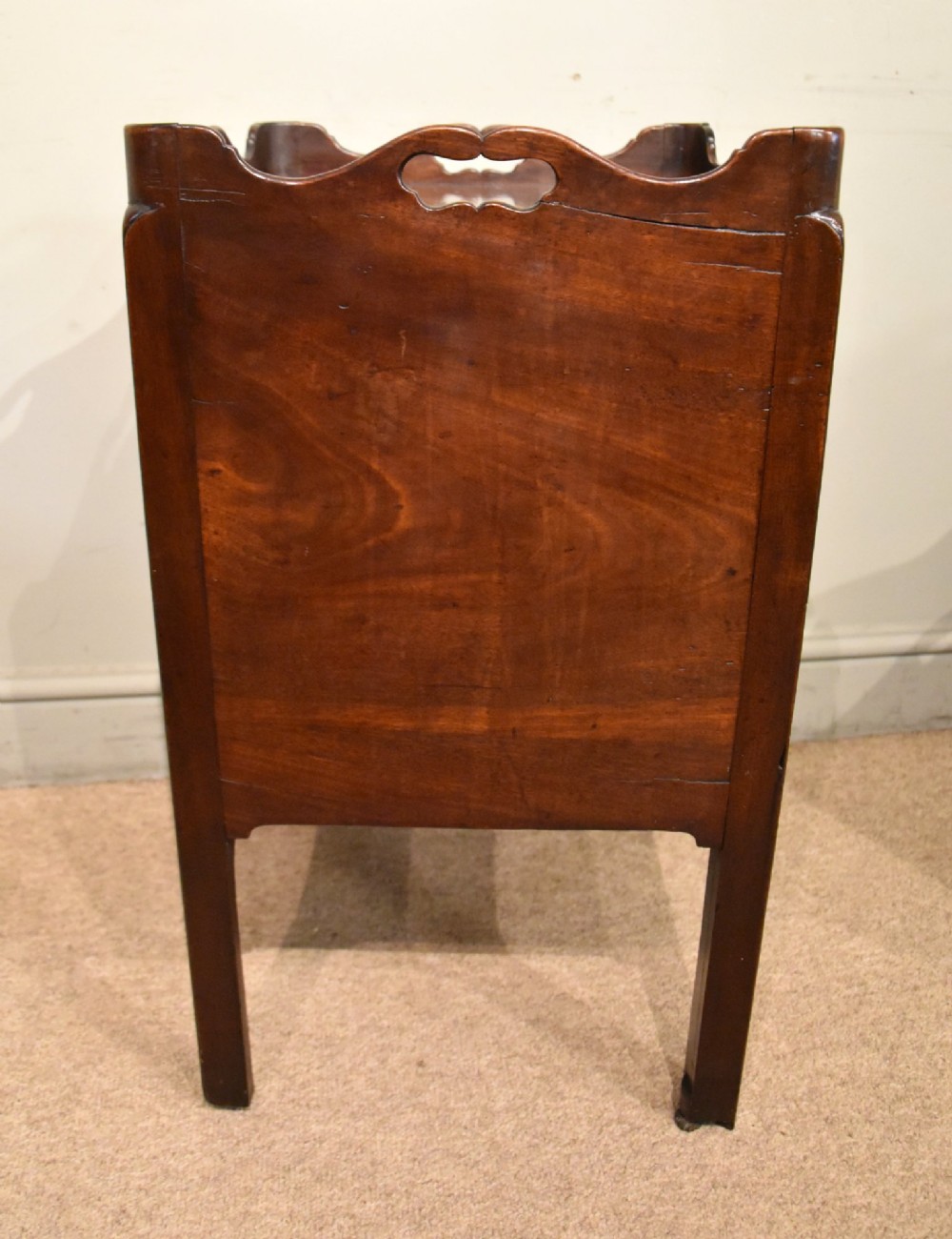 A matched pair of dark mahogany Georgian bedside cabinets, each featuring a shaped gallery top with cutout handles, a two-door cabinet, and a single lower drawer with a brass handle. View V