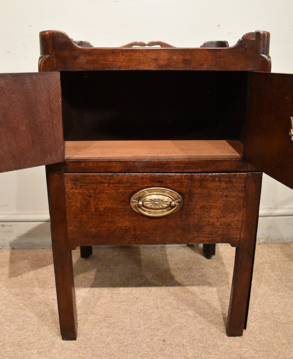A matched pair of dark mahogany Georgian bedside cabinets, each featuring a shaped gallery top with cutout handles, a two-door cabinet, and a single lower drawer with a brass handle. View VI