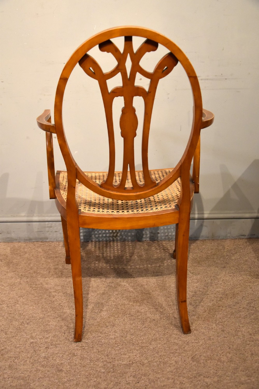 An Edwardian satinwood open armchair featuring an oval pierced backrest, hand-painted floral motifs, sweeping arms, and a woven cane seat. View V