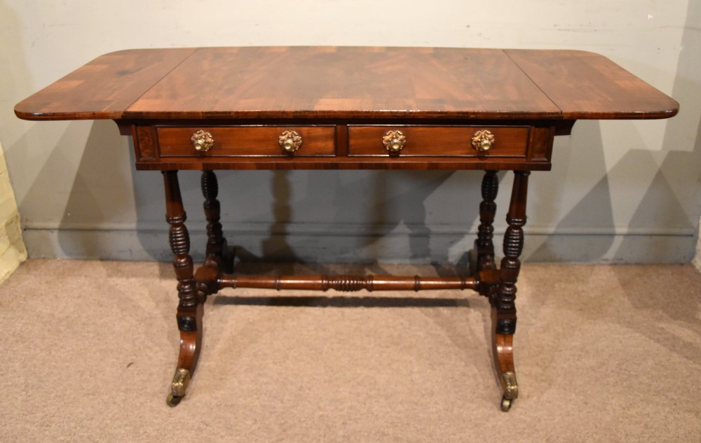 Regency flame mahogany sofa table featuring two drop leaves, two frieze drawers with brass handles, turned double supports, a central stretcher, and brass castors. View III