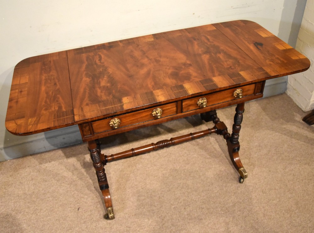 Regency flame mahogany sofa table featuring two drop leaves, two frieze drawers with brass handles, turned double supports, a central stretcher, and brass castors. View VI