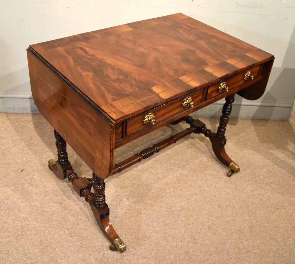 Regency flame mahogany sofa table featuring two drop leaves, two frieze drawers with brass handles, turned double supports, a central stretcher, and brass castors. View VII