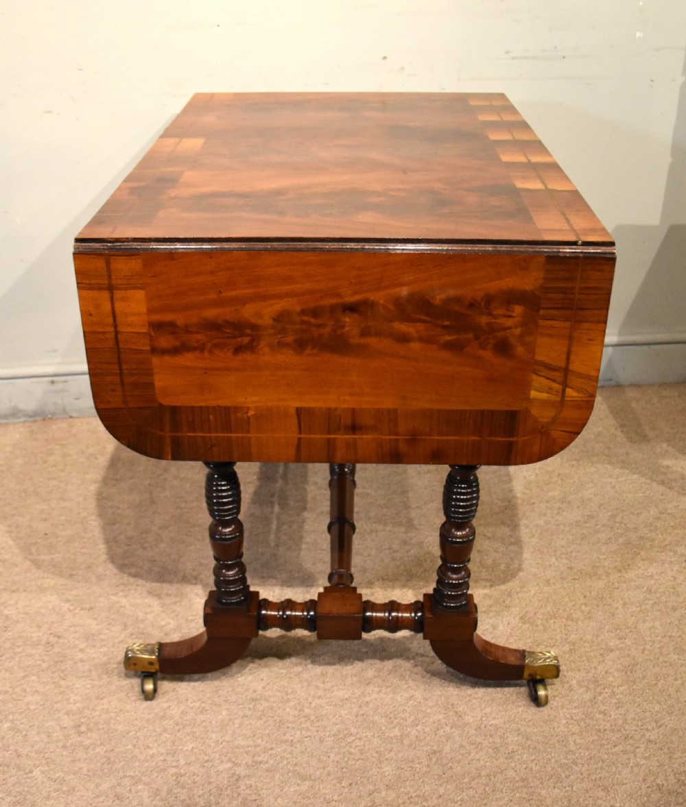 Regency flame mahogany sofa table featuring two drop leaves, two frieze drawers with brass handles, turned double supports, a central stretcher, and brass castors. View VIII