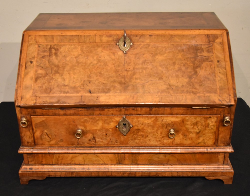 A George I period burr walnut travelling writing bureau with a sloped fall-front lid, lower drawer, and brass escutcheons.