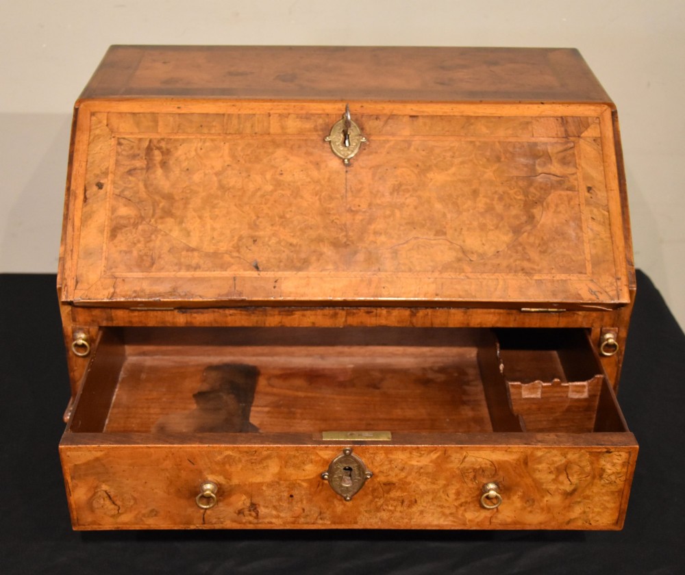 A George I period burr walnut travelling writing bureau with a sloped fall-front lid, lower drawer, and brass escutcheons. View II