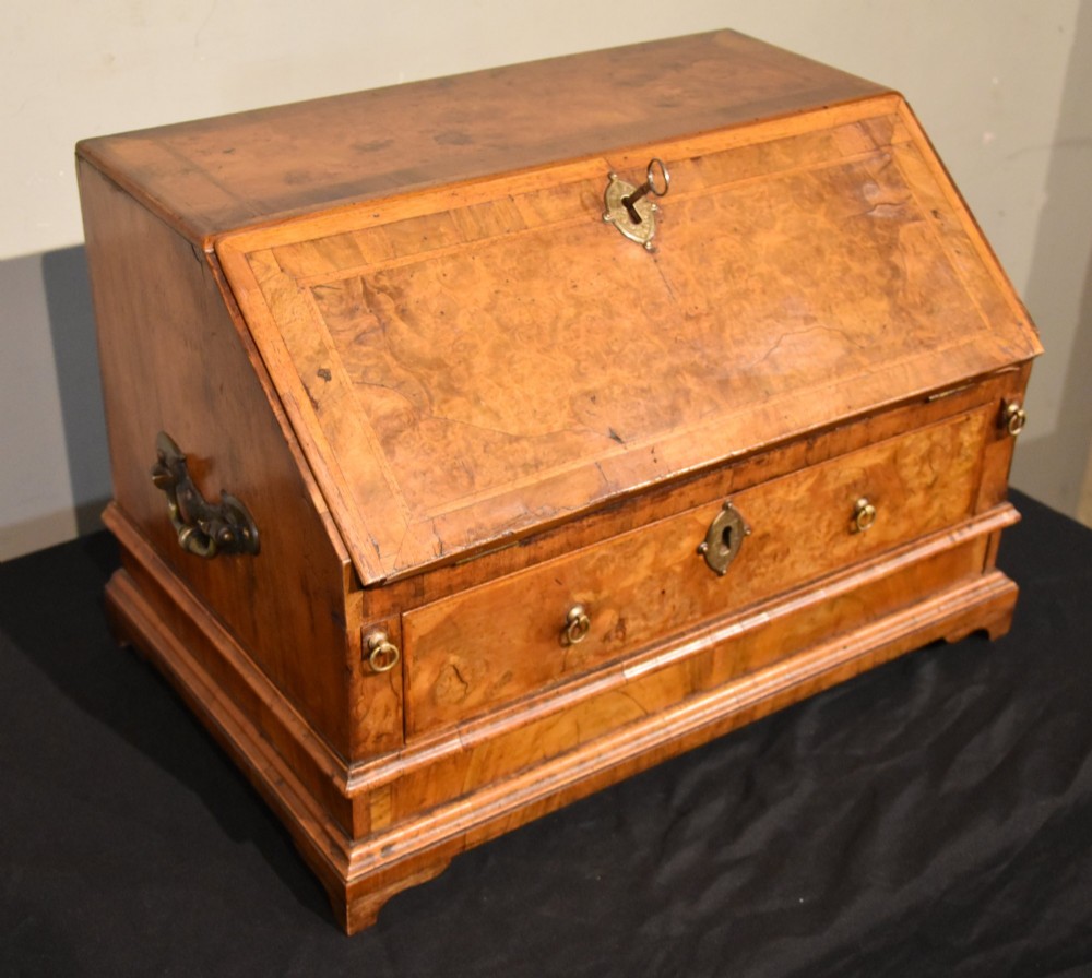 A George I period burr walnut travelling writing bureau with a sloped fall-front lid, lower drawer, and brass escutcheons. View V