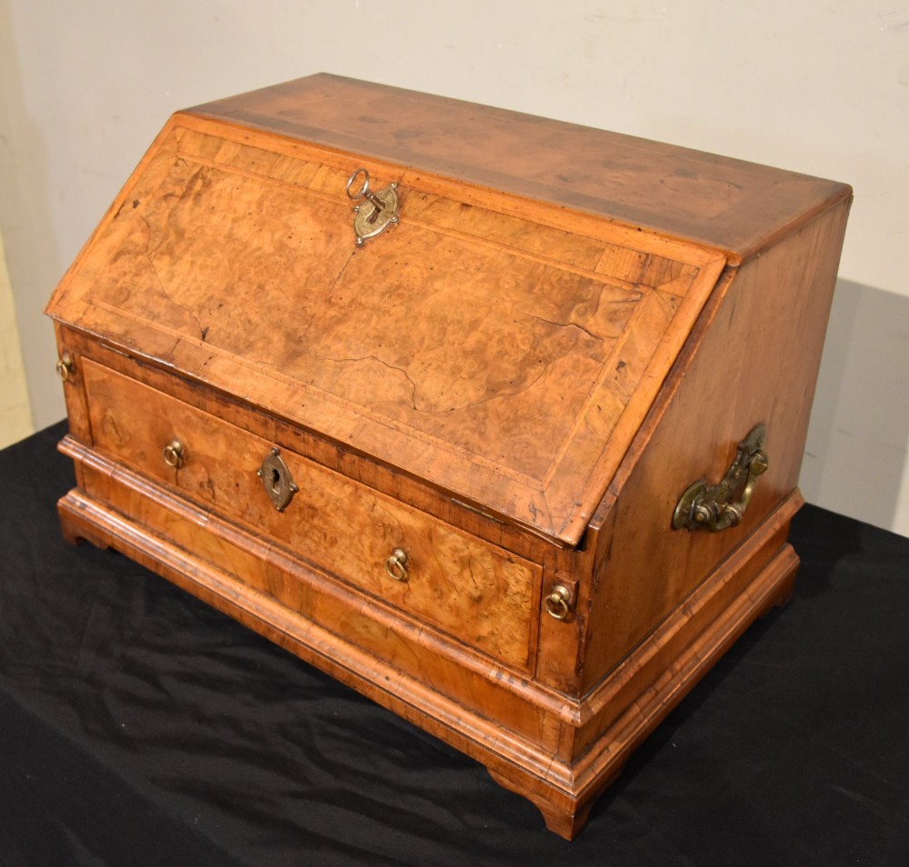 A George I period burr walnut travelling writing bureau with a sloped fall-front lid, lower drawer, and brass escutcheons. View VI