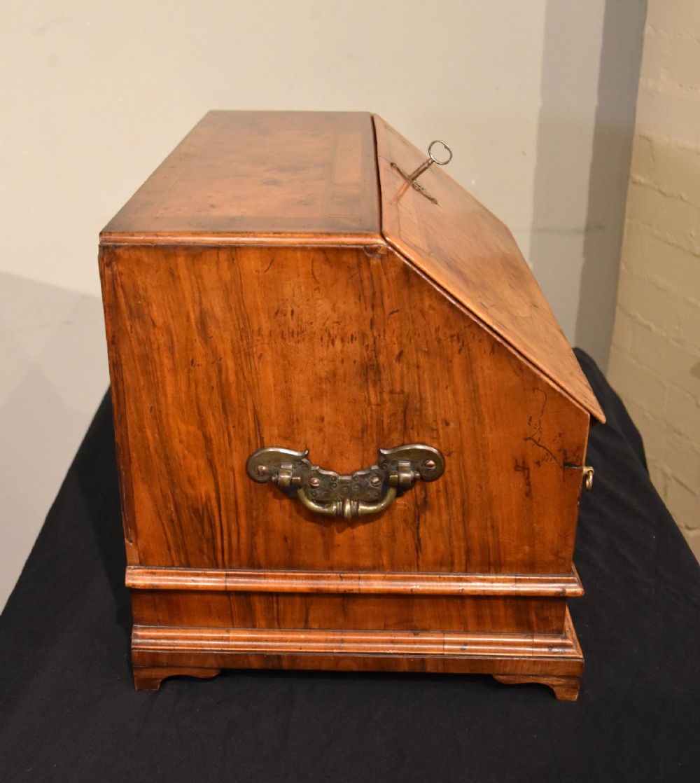 A George I period burr walnut travelling writing bureau with a sloped fall-front lid, lower drawer, and brass escutcheons. View VII