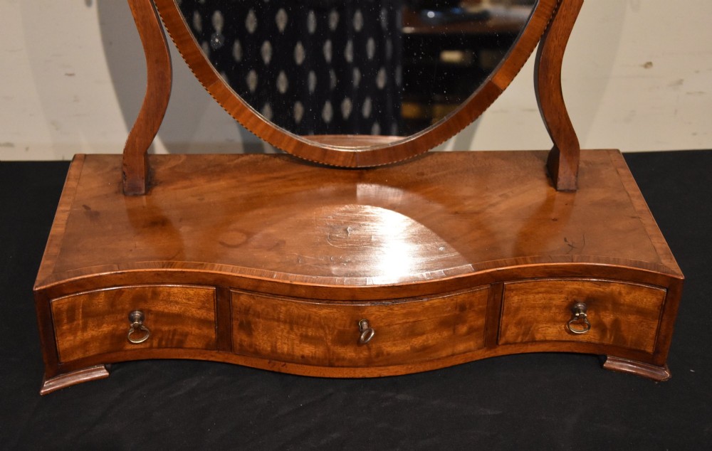 A Georgian mahogany dressing mirror featuring an oval adjustable mirror supported by curved uprights above a serpentine-fronted base with three small drawers. View III