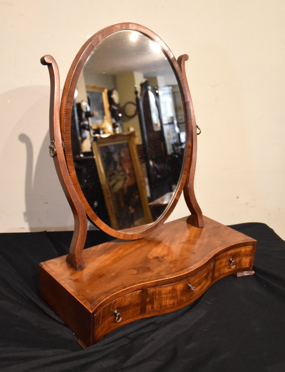A Georgian mahogany dressing mirror featuring an oval adjustable mirror supported by curved uprights above a serpentine-fronted base with three small drawers. View V