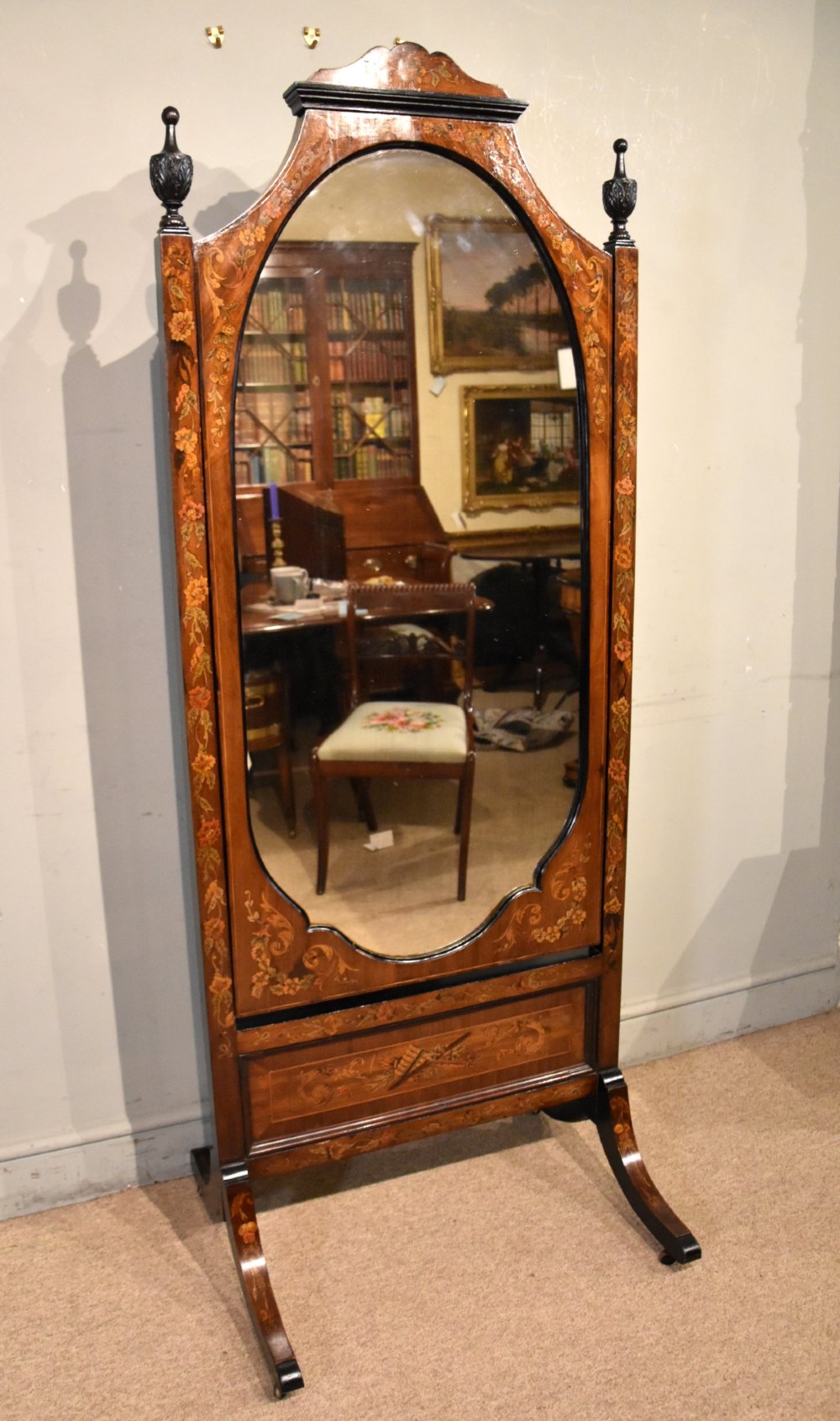 A Victorian mahogany cheval mirror featuring detailed floral marquetry inlays, carved urn finials, an arched glass frame, and splayed feet.