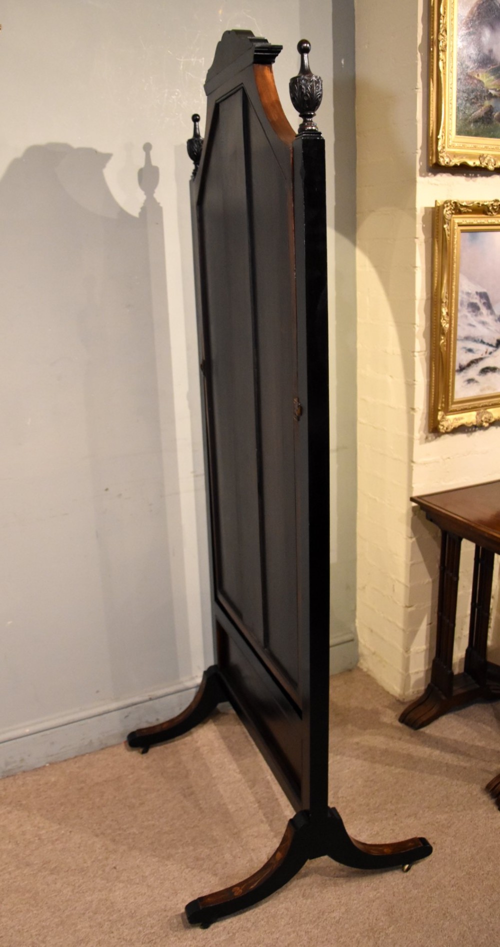 A Victorian mahogany cheval mirror featuring detailed floral marquetry inlays, carved urn finials, an arched glass frame, and splayed feet. View X