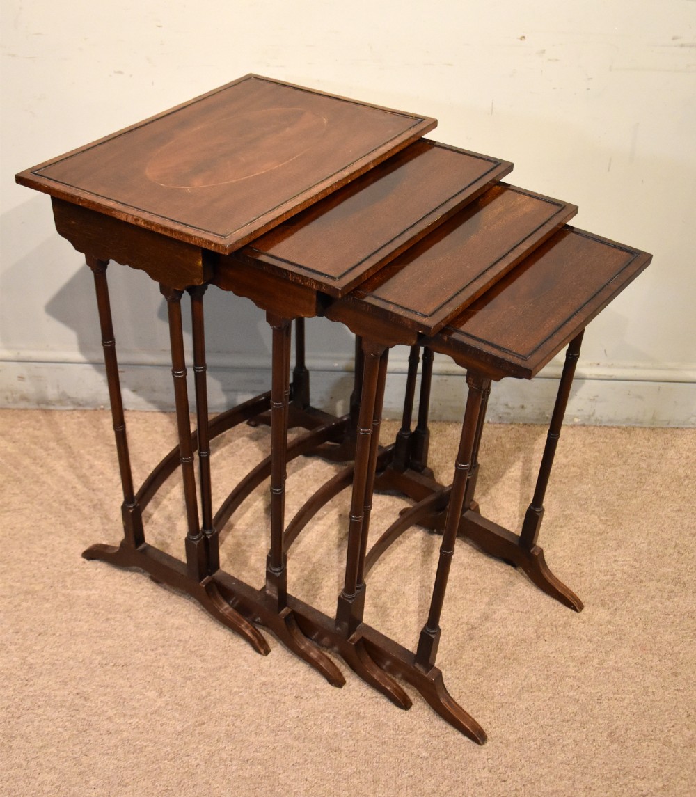 A set of four graduated Edwardian mahogany nest tables displayed in a stepped formation, featuring turned legs and an oval inlaid top.