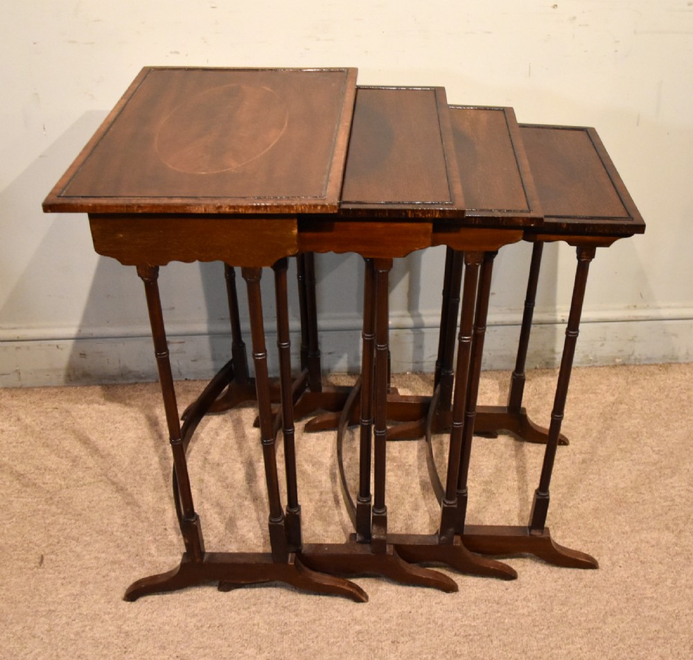 A set of four graduated Edwardian mahogany nest tables displayed in a stepped formation, featuring turned legs and an oval inlaid top. View II