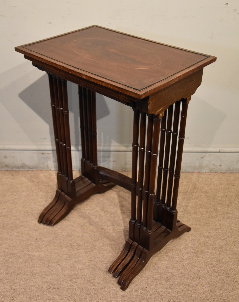 A set of four graduated Edwardian mahogany nest tables displayed in a stepped formation, featuring turned legs and an oval inlaid top. View IV