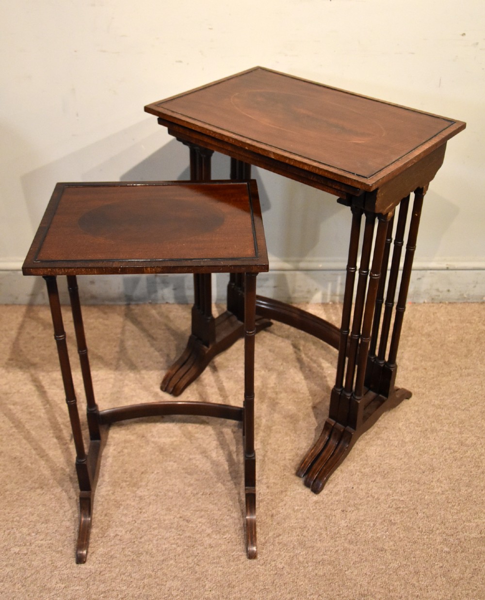 A set of four graduated Edwardian mahogany nest tables displayed in a stepped formation, featuring turned legs and an oval inlaid top. View V