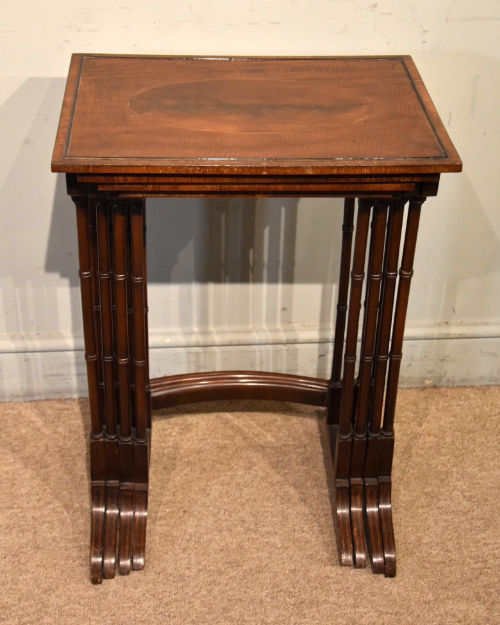 A set of four graduated Edwardian mahogany nest tables displayed in a stepped formation, featuring turned legs and an oval inlaid top. View VI