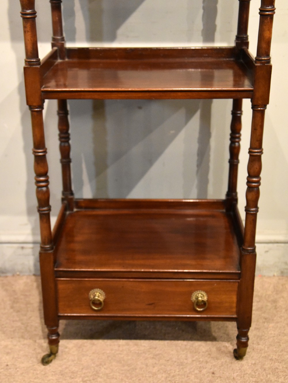 A late nineteenth-century mahogany four-tier whatnot featuring turned spindle supports, a lower drawer with brass ring handles, and brass casters. View II