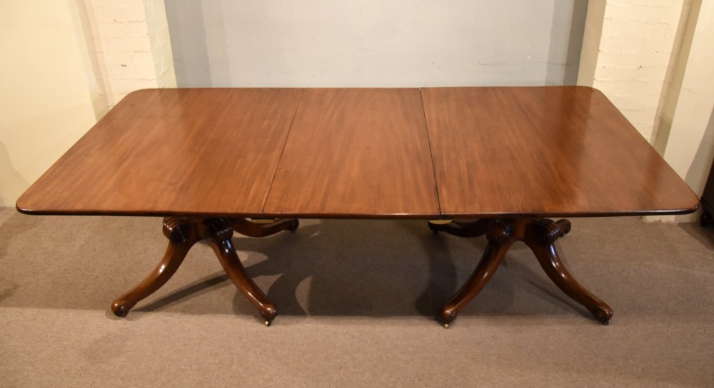 A Regency period mahogany extending dining table supported by two turned pedestal bases with reeded splayed legs and brass castors. View II