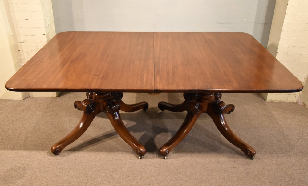 A Regency period mahogany extending dining table supported by two turned pedestal bases with reeded splayed legs and brass castors. View IV