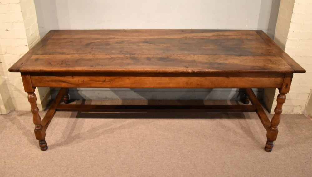 A 19th-century French walnut farmhouse dining table featuring a wide plank top, plain frieze, turned legs, and a low H-stretcher.