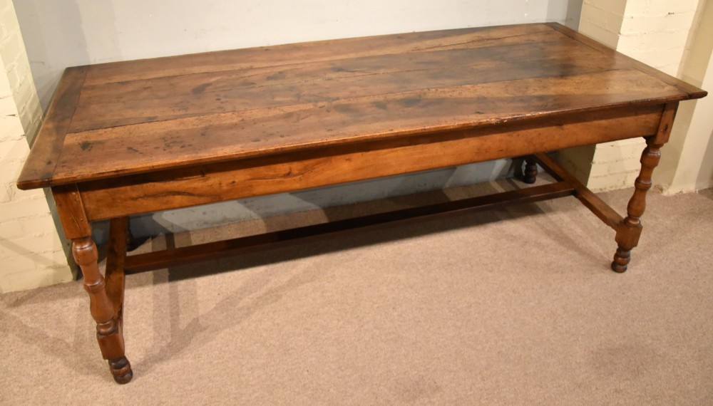 A 19th-century French walnut farmhouse dining table featuring a wide plank top, plain frieze, turned legs, and a low H-stretcher. View II