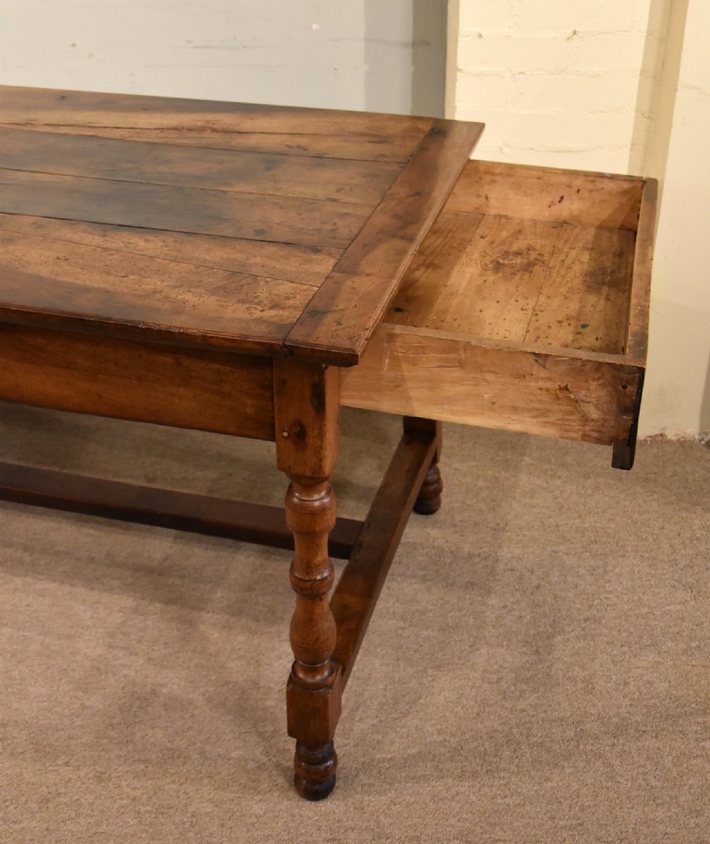 A 19th-century French walnut farmhouse dining table featuring a wide plank top, plain frieze, turned legs, and a low H-stretcher. View IV
