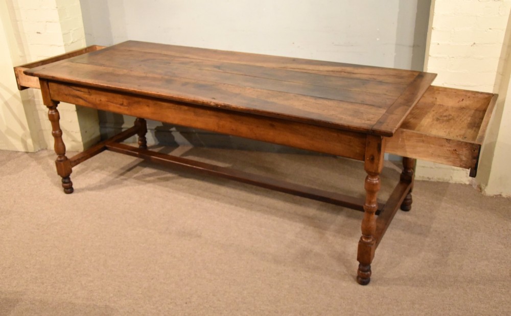 A 19th-century French walnut farmhouse dining table featuring a wide plank top, plain frieze, turned legs, and a low H-stretcher. View V