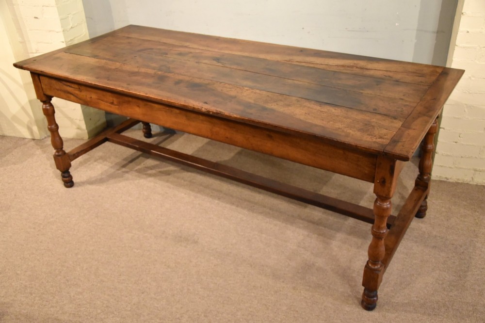 A 19th-century French walnut farmhouse dining table featuring a wide plank top, plain frieze, turned legs, and a low H-stretcher. View VI