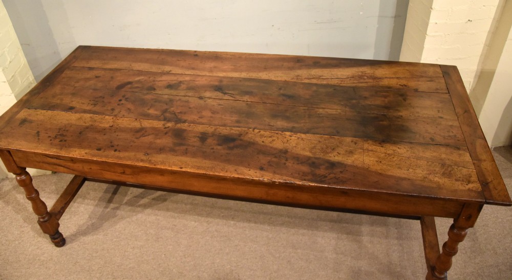 A 19th-century French walnut farmhouse dining table featuring a wide plank top, plain frieze, turned legs, and a low H-stretcher. View VII