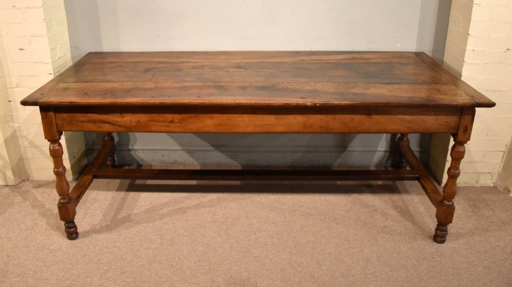 A 19th-century French walnut farmhouse dining table featuring a wide plank top, plain frieze, turned legs, and a low H-stretcher. View VIII