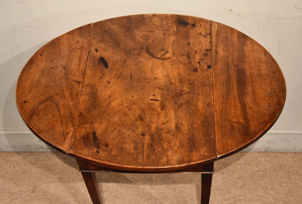 An 18th-century Georgian mahogany Pembroke table featuring an oval drop-leaf top, a frieze drawer with a brass handle, and four square tapered legs. View V