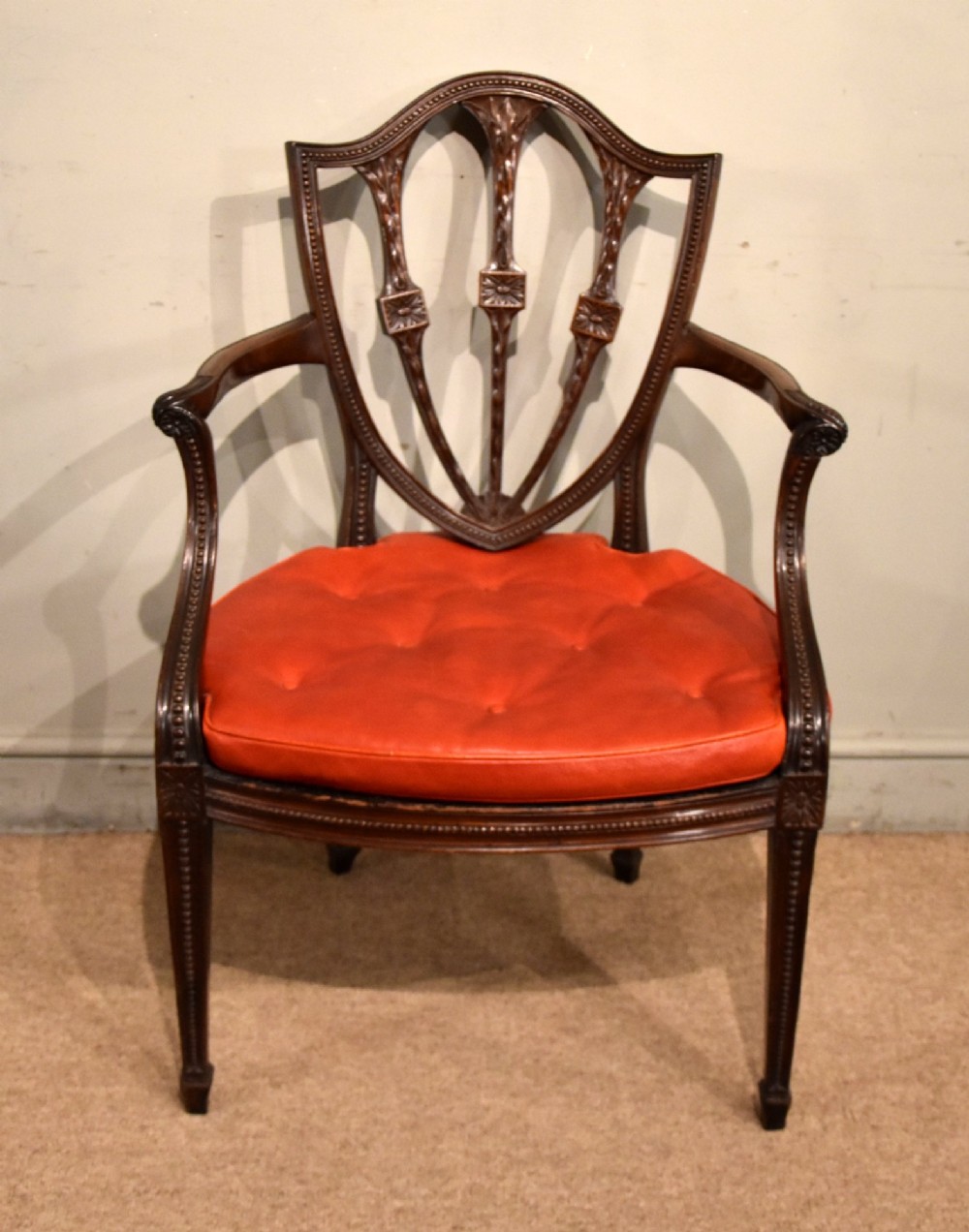 An 18th-century George III carved mahogany armchair featuring a shield-shaped open backrest, swept armrests, and a button-tufted red leather seat cushion.