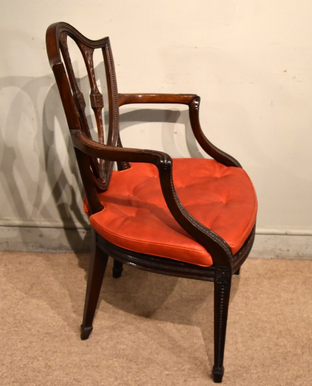 An 18th-century George III carved mahogany armchair featuring a shield-shaped open backrest, swept armrests, and a button-tufted red leather seat cushion. View II