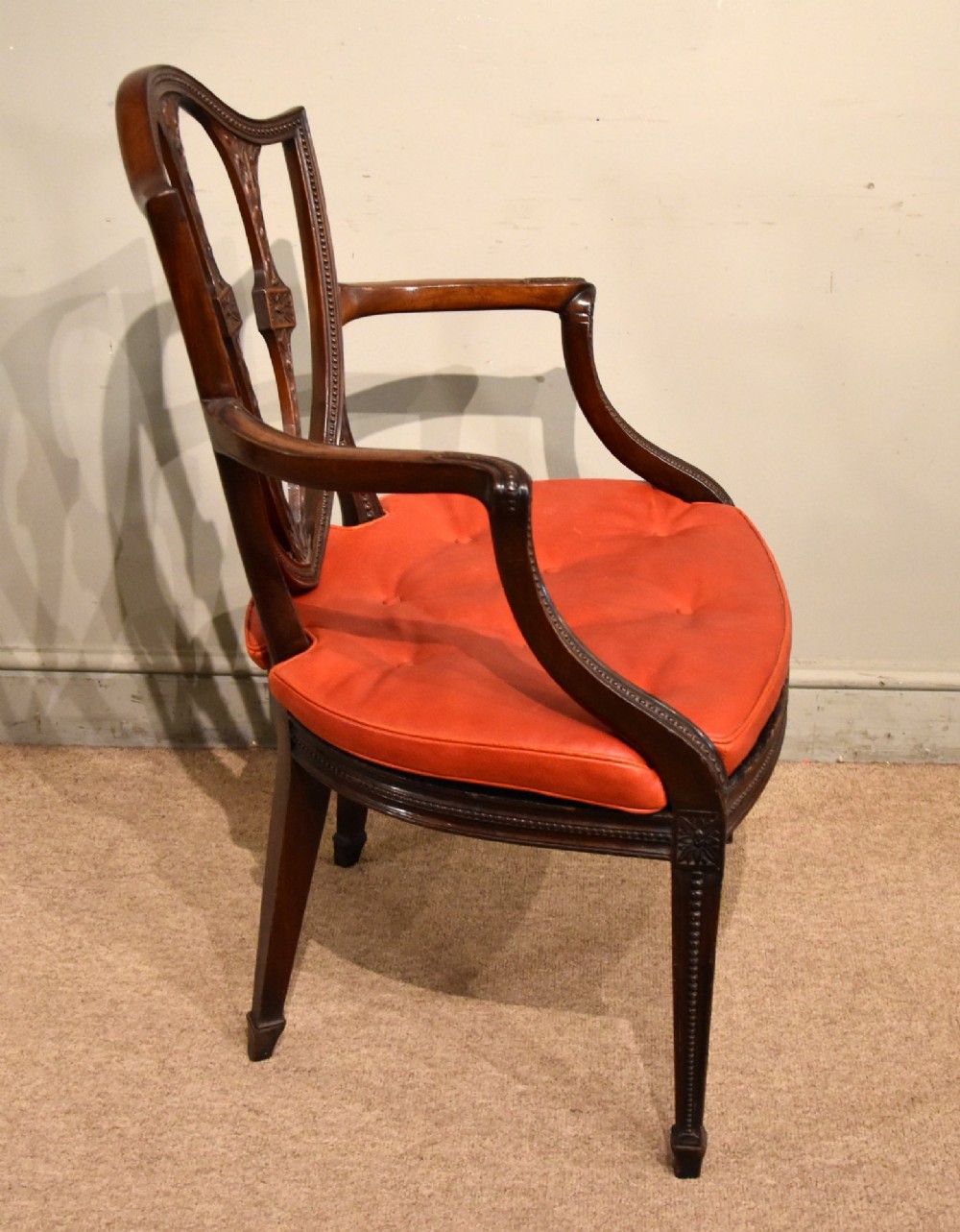 An 18th-century George III carved mahogany armchair featuring a shield-shaped open backrest, swept armrests, and a button-tufted red leather seat cushion. View IV